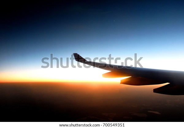 View from a cabin of a plane, overlooking Sun\
rise, splitting dark blue sky with a horizontal line of Sun ray in\
orange, dividing a dark shade\
below