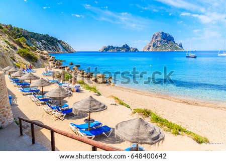 View of Cala d'Hort beach with sunbeds and umbrellas and beautiful azure blue sea water, Ibiza island, Spain