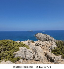 A view of calm blue sea waves lapping against a rocky shoreline beneath a clear sky. - Powered by Shutterstock