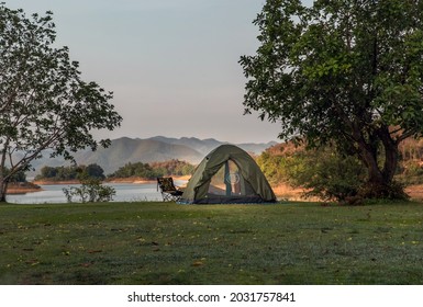 View of a camping tent on the dry ground Near beautiful big tree at the campsite in lake shore with mountain range in background. No focus, specifically. - Shutterstock ID 2031757841