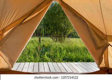 View from the canvas tent upon the green meadow with trees. POV