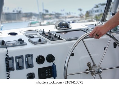 A view of the captain's hand using the steering wheel in the helm of a boat.