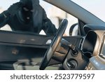 View from the car at the man dressed in black with a balaclava on his head looking at the glass of car before the stealing. Car thief, car theft concept