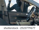 View from the car at the man dressed in black with a balaclava on his head preparing breaking with crowbar the glass of car before the stealing. Car thief, car theft concept