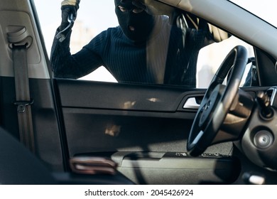 View from the car at the man dressed in black with a balaclava on his head preparing breaking with crowbar the glass of car before the stealing. Car thief, car theft concept 