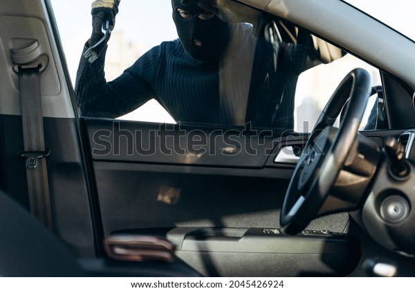 View from the car\
at the man dressed in black with a balaclava on his head preparing\
breaking with crowbar the glass of car before the stealing. Car\
thief, car theft concept 