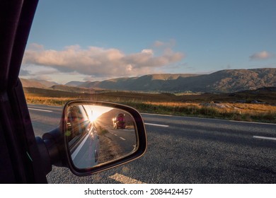 View From A Car On A Mountains And Reflection In Car Mirror Of Sun Rise Over Mountain Peak And Concrete Mixer Truck Passing By. Connemara, County Galway, Ireland. Car Travel With Stunning Scenery.