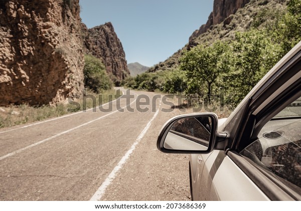 View from the car on the side of\
the road to the rearview mirror and the winding mountain\
road