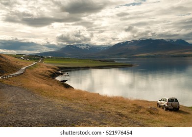View of a car parked on a lakeside near the main road leading to a mountain range in Iceland.