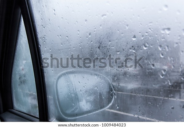 View of a car side mirror from inside
the car with condensation and rain on the glass
window