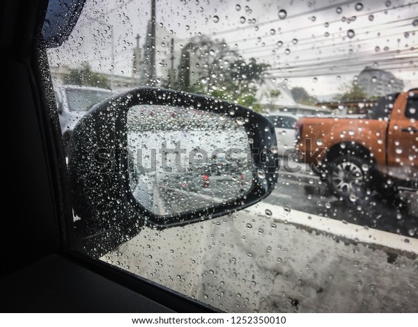 View of a car side mirror from\
inside the car with and rain on the glass window,Rain on working\
day