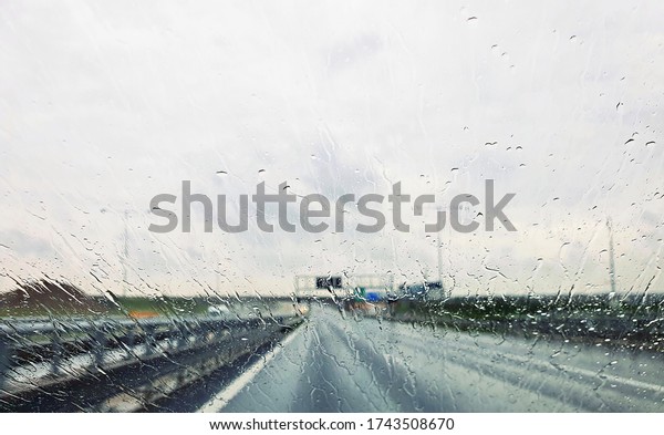 A view from car\
through window with rain drops during riding. Driving a car in the\
rain storm on highway.