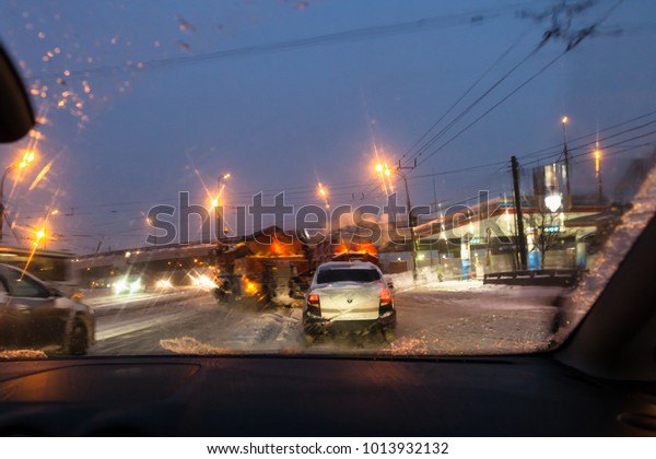 view of car traffic and street sweeping machines\
through wet windscreen while driving car on road in Moscow city in\
winter evening in snow