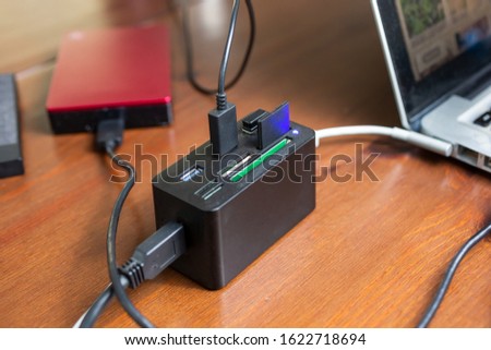 A view of a card reader and port hub connected to a laptop computer, featuring external hard drives, storage cards and cables.