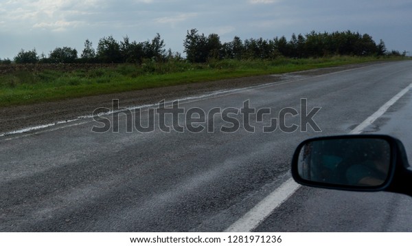 A view from the car\'s\
interior to the mirror driving, the automobile road after rain and\
green trees.