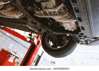 View of a car's underbody on a lift in a repair shop, showcasing mechanical parts and structures. Perfect for automotive and maintenance themes. - Powered by Shutterstock