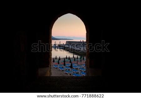 View of Cefalu Harbour wall during sunset through an archway, Cefalu, Sicily, Italy - June 2015