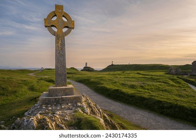 View of Celtic Cross on Ynys Llanddwyn Island in Angelsey with Twr Mawr Lighthouse in background landscape