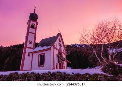 View of the church of Saint John (San Giovanni) in the sunset with purple sky in the Funes Valley, village of Saint Magdalena (Santa Maddalena), Trentino Alto Adige, South Tyrol, Italy.