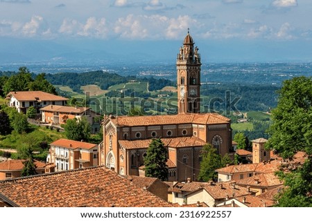 View of the church with tall belfry among old houses with red roofs in small town of Monforte d'Alba in Piedmont, Italy.