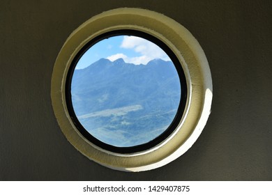 A view from a circular window of a building overlooking a mountain range.