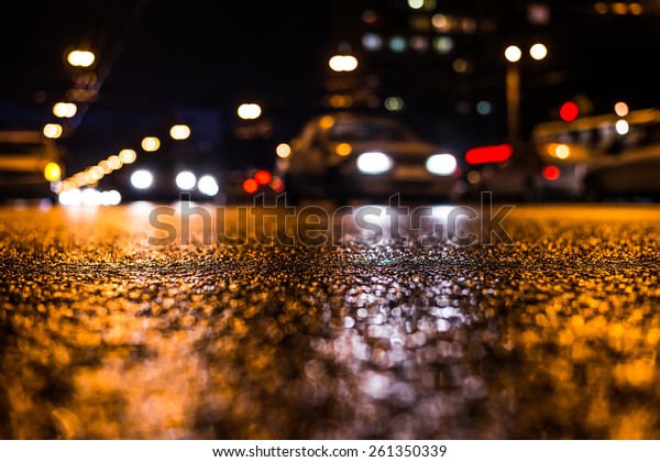 View of the city at\
night after the rain, the cars driving on the road. View from the\
level of asphalt level