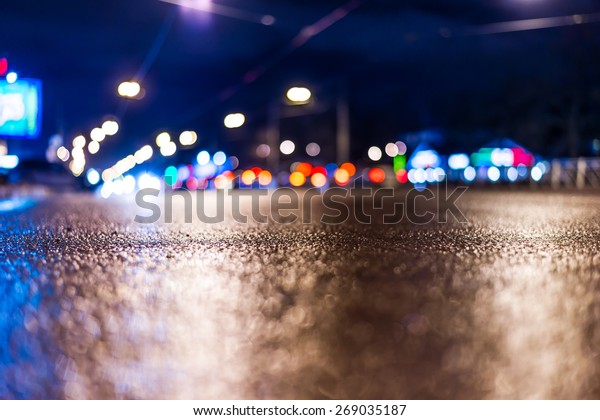 View of the city at night after the rain, the\
cars driving on the road and shine the headlights. View from the\
level of asphalt level, in blue\
tones