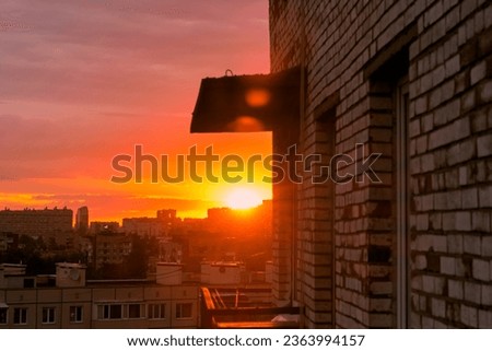 View of the city in sunset light from the balcony of an old brick house. The sun sets over the horizon, backlight.