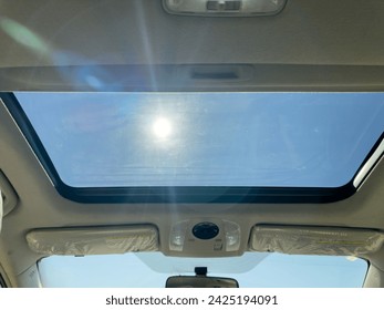 View of the clear sky through the open sunroof hatch of a car on a sunny day.