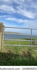 View of cliffs and the Atlantic Ocean over green fields and seen through a silver metal gate in Cork, Ireland