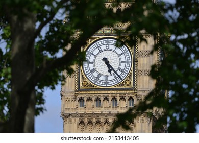 View of the clock face of Big Ben framed by green leafy trees at the Houses of Parliament in Westminster London