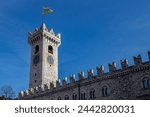 View of Clock Tower (Torre Civica or Torre di Piazza), Trento flag and walls of Palazzo Pretorio in a sunny day; Trento, Trentino-Alto Adige, Italy