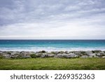 View of the cloudy sea at qixingtan beach on the coast of Hualien Taiwan. Frontal view with a green strip of meadow in the foreground and round rocks behind.