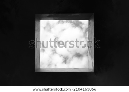 view of the cloudy sky through a square skylight in black and white