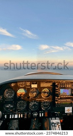 View from the cockpit of a small propeller plane that can carry two people. Flight information from various instrument panels and display in the middle of the aircraft and propeller visible in window.