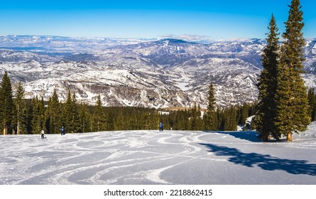 View of Colorado ski slope near Aspen, Colorado, with ski tracks on foreground and mountain range in background on sunny winter day