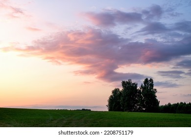 View of a colorful bright summer sunset with beautiful clouds and sun rays with a large grassy field in the foreground and trees on the horizon. - Powered by Shutterstock