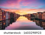 View of colorful timber houses surrounding river Nidelva in the city of Trondheim at sunset. View from Old Town Bridge. Trondelag county. Norway