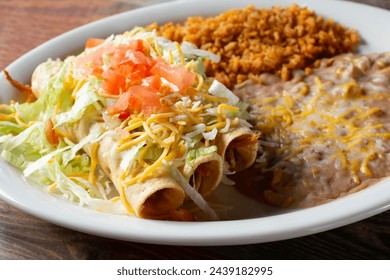 A view of a combo plate with three taquitos, rice and beans.
