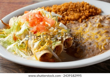 A view of a combo plate with three taquitos, rice and beans.