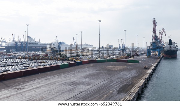 View of a commercial harbor with a docking ship and\
a huge car park.