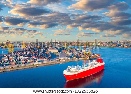 View commercial sea port on a Sunny day. Cargo ship Red against blue water. Transportation of goods by water transport. Berth with colorful containers. Commercial port infrastructure.