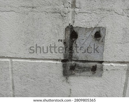 Close‑up view of a concrete block wall featuring a square metal plate secured with four rusted bolts.