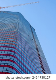 View of the construction of a skyscraper from the bottom up. The crane is attached to a tall building. Construction industry. Modern glass skyscraper almost completed