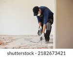 View of a construction worker using a hand-held demolition hammer and breaker to demolish walls to remove old floor tiles during renovation work.