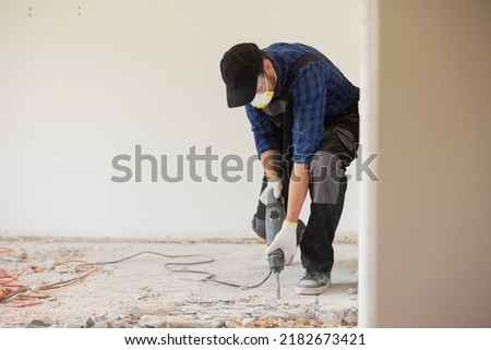 View of a construction worker using a hand-held demolition hammer and breaker to demolish walls to remove old floor tiles during renovation work.