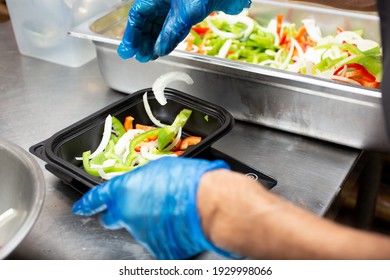 A View Of A Cook Preparing Vegetable Ingredients Into A Meal Prep Container, In A Restaurant Kitchen Setting.