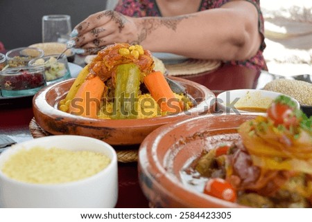 View of cous cous with vegetables and a tajine while a hennaed hand is served