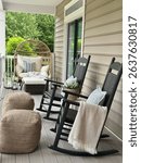 View of a cozy porch with black rocking chairs, an oversized egg chair, fluffy pillows and a soft blanket against a summer green backdrop, perfect for relaxing.