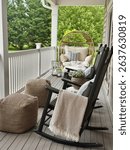 View of a cozy porch with black rocking chairs, an oversized egg chair, fluffy pillows and a soft blanket against a summer green backdrop, perfect for relaxing.